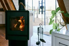 Un poêle à bois MCZ crépitant dans un chalet moderne, avec une grande baie vitrée donnant sur la forêt. Un avis positif s'impose pour ce coin cosy.