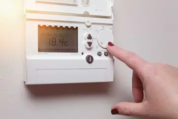 Main d'une femme ajustant un cee thermostat connecté affichant 18.4°C.