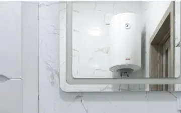 Gros chauffe-eau blanc, une chaudière micro accumulation, reflété dans un grand miroir, sur fond de carrelage marbré.