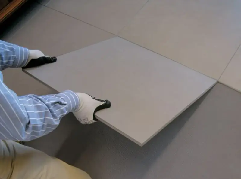 Pose d'une nouvelle dalle pour coller du carrelage sur du carrelage. Les mains gantées ajustent la pièce sur le sol existant.