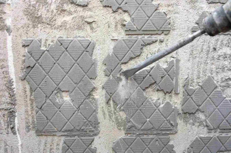 Outil de burinage en action pour enlever colle carrelage sur un mur en béton.